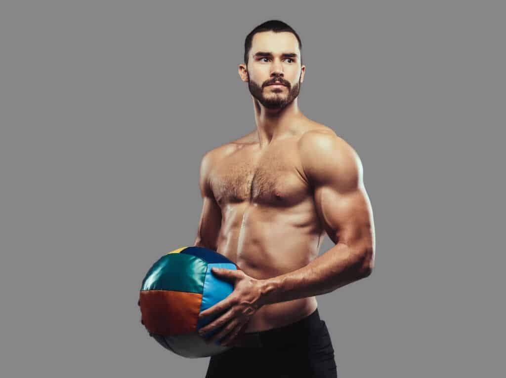 A brutal athletic bearded shirtless male posing with a medball o