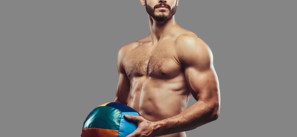 A brutal athletic bearded shirtless male posing with a medball o