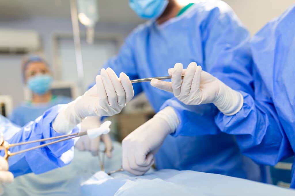 Low Angle Shot in the Operating Room, Assistant Hands out Instruments to Surgeons During Operation. Surgeons Perform Operation. Professional Medical Doctors Performing Surgery.