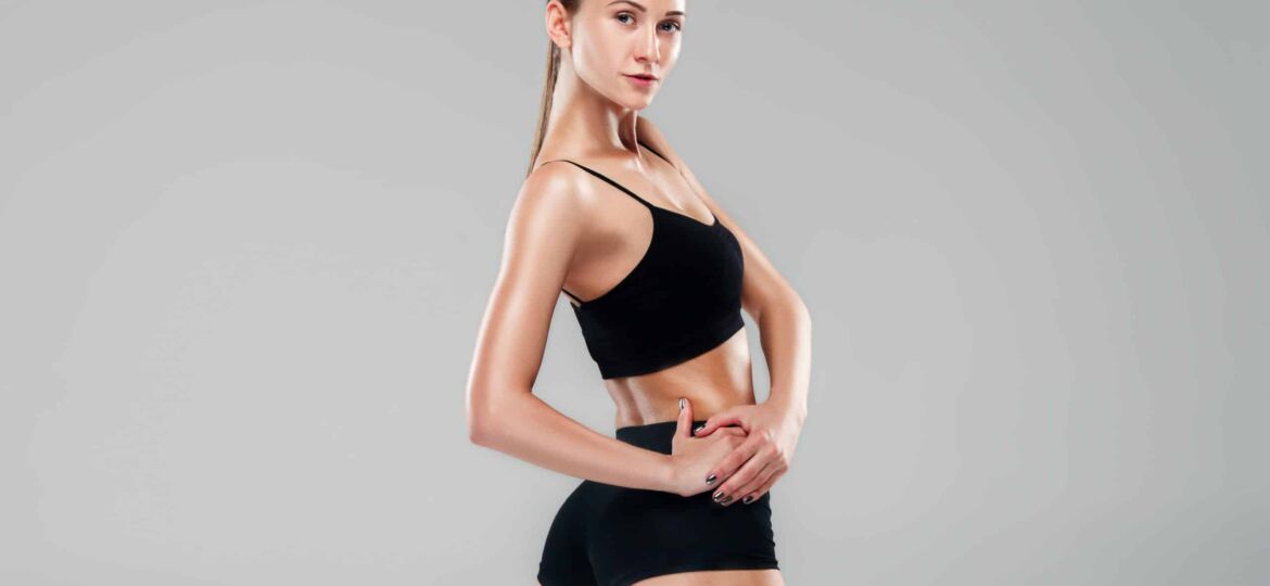 Muscular young woman athlete posing on gray studio background