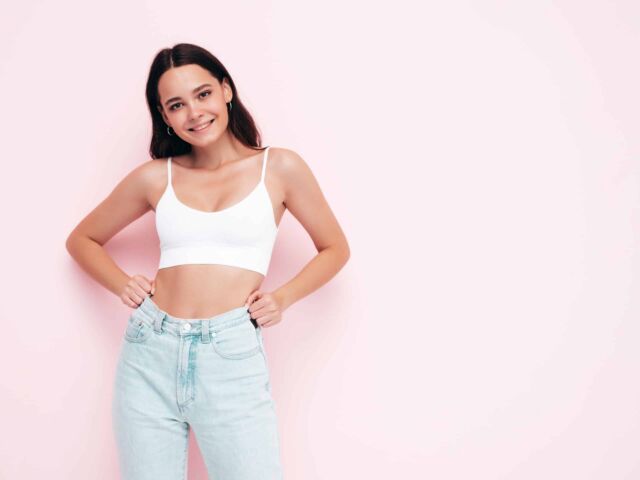 Young beautiful smiling female in trendy summer clothes. Sexy carefree woman posing near pink wall in studio. Positive brunette model having fun and going crazy. Cheerful and happy