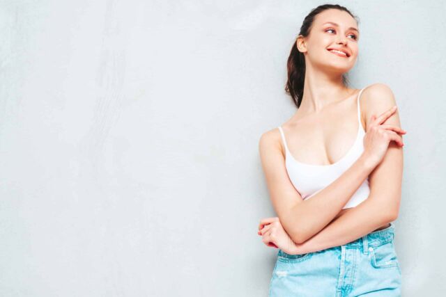 Young beautiful smiling female in trendy summer jeans skirt and top. Sexy carefree woman posing near grey wall in studio. Positive brunette model having fun and going crazy. Cheerful and happy