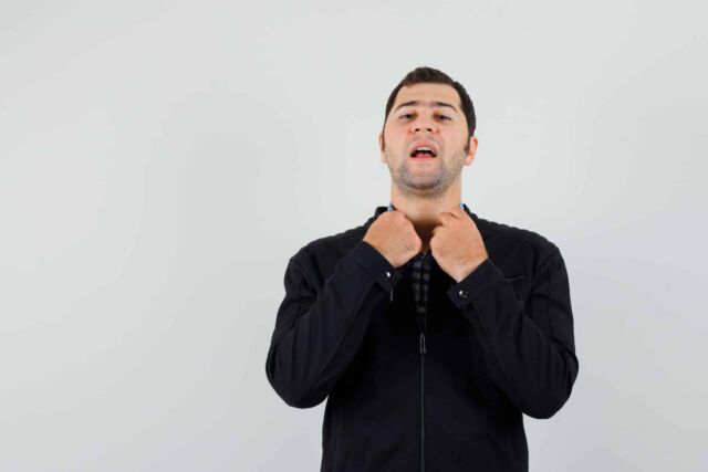 Young man holding collar of his shirt in shirt, jacket and looki