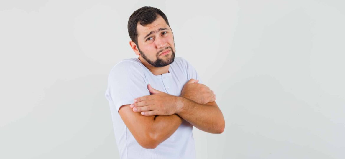 Young man hugging himself in t-shirt and looking cold. front view.