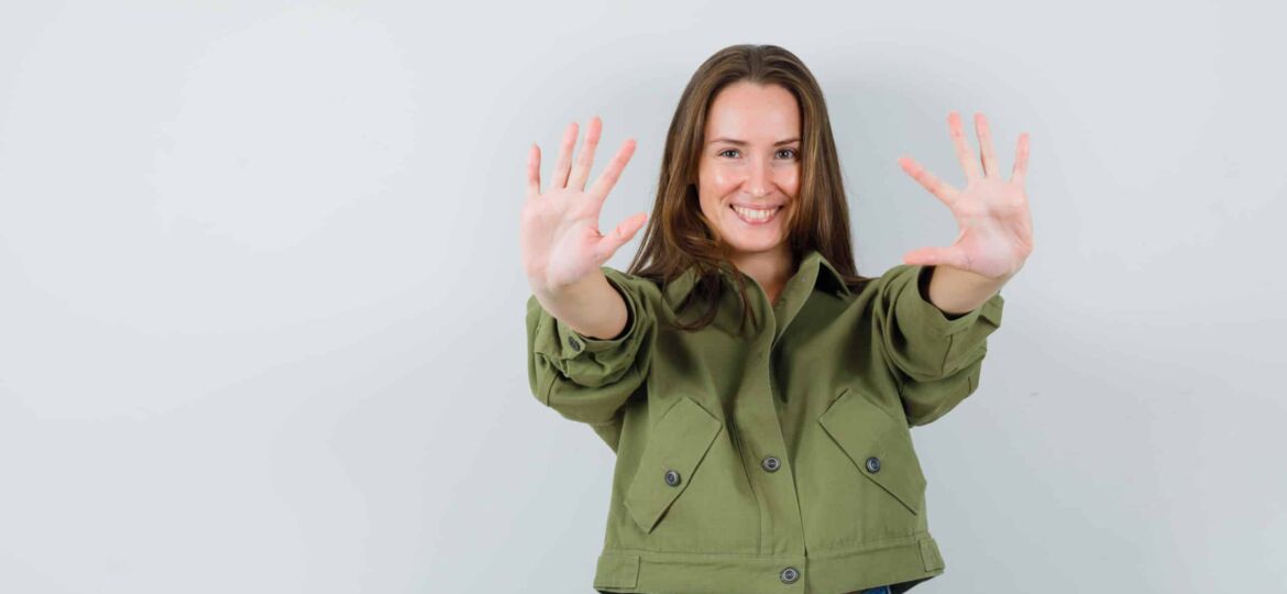 Young girl in jacket, shorts showing ten fingers and looking jol