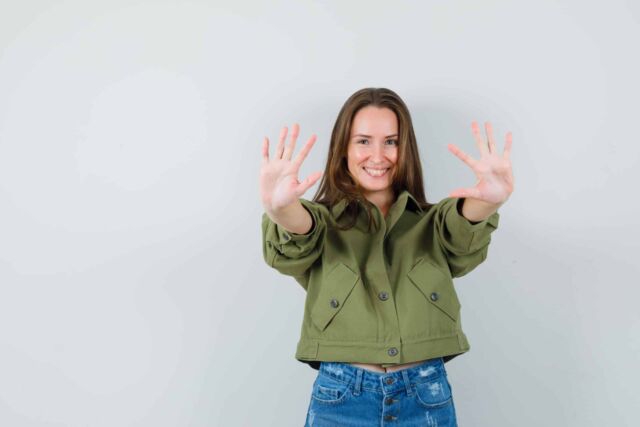 Young girl in jacket, shorts showing ten fingers and looking jol