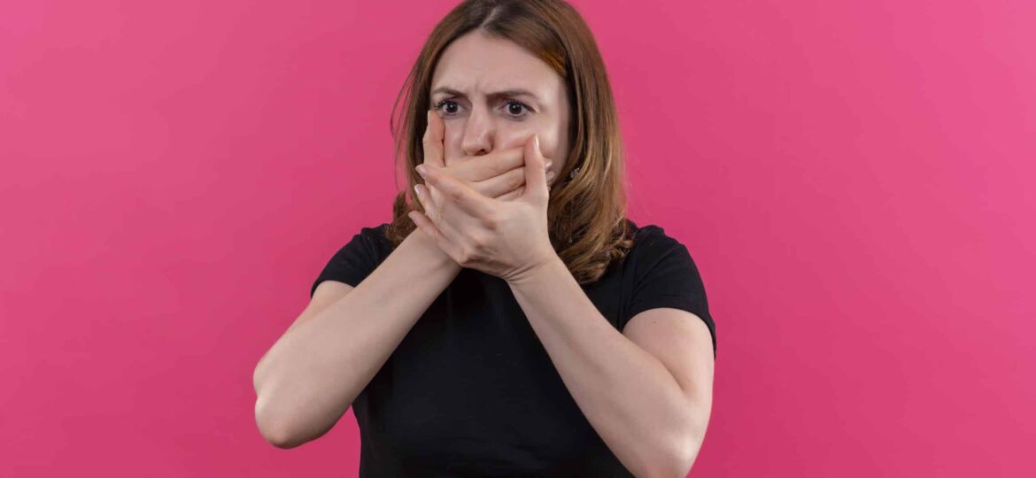 anxious young casual woman with hands on mouth on isolated pink background with copy space