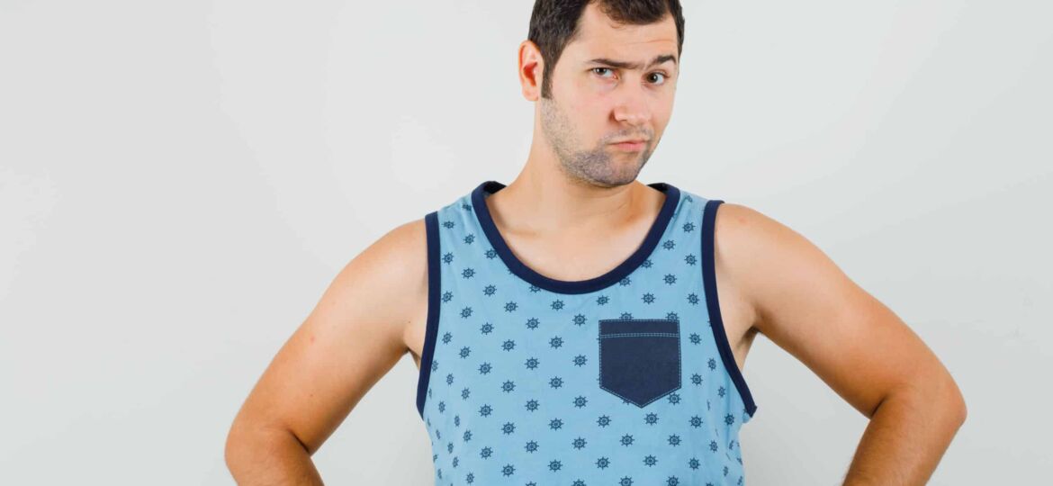 Young man in blue singlet looking at camera while frowning and looking pensive , front view.
