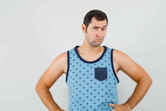 Young man in blue singlet looking at camera while frowning and looking pensive , front view.