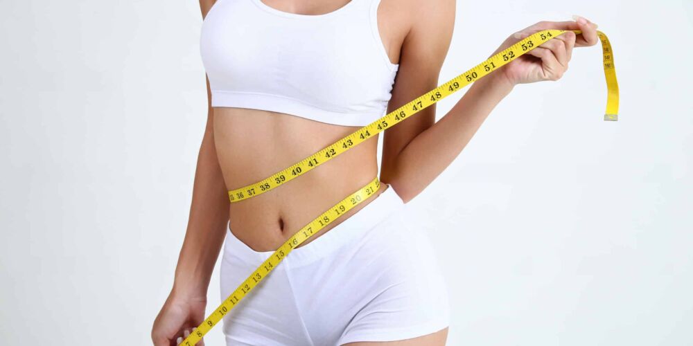 Close up slimming female with beautiful body and measuring her waistline  with measure tape on white background and copy space