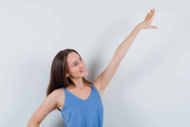 young lady stretching arm in singlet, skirt and looking cheerful , front view.