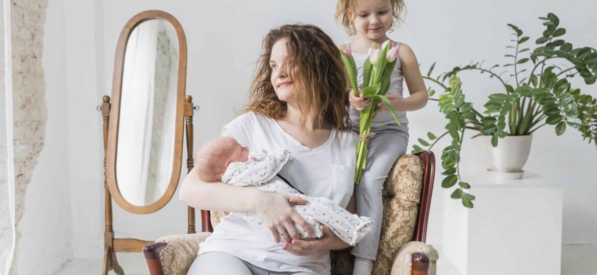 madre-feliz-que-se-sienta-en-la-silla-del-brazo-con-su-nino-lindo-dos-en-casa