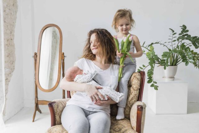 madre-feliz-que-se-sienta-en-la-silla-del-brazo-con-su-nino-lindo-dos-en-casa